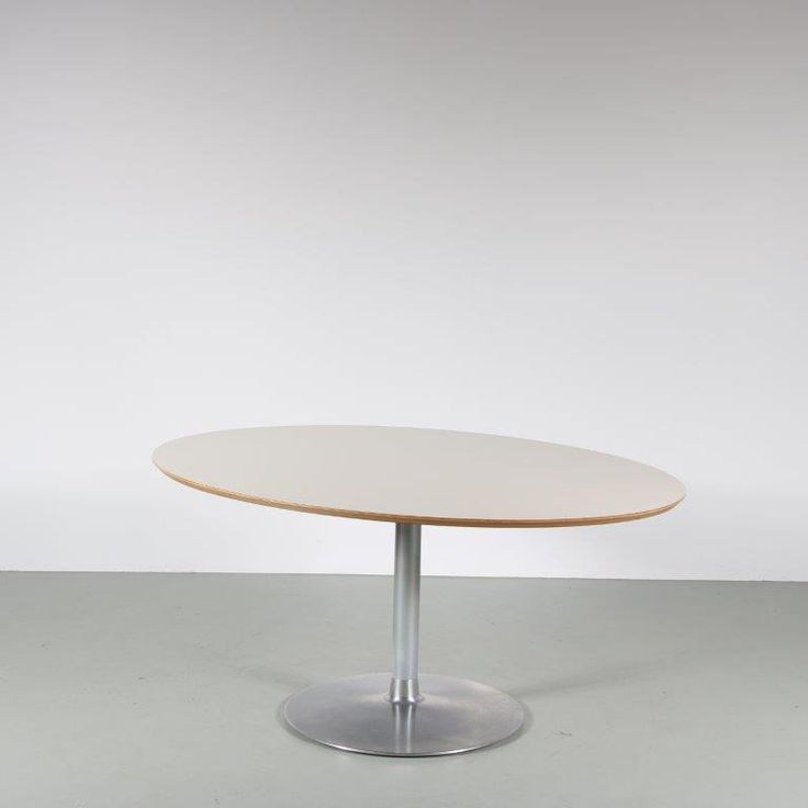 a white table with a silver base on a gray floor in front of a white wall