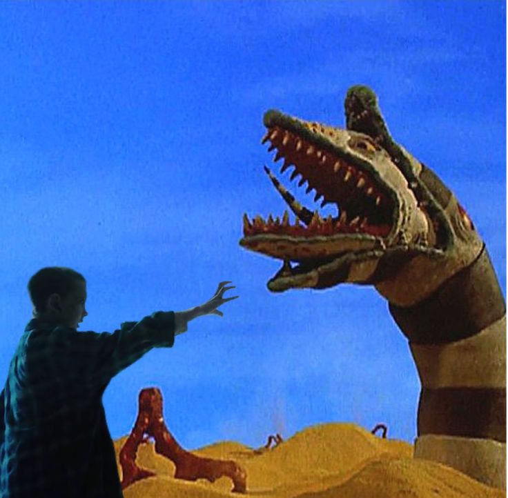 a man standing in front of a fake t - rex with his hand out to another person