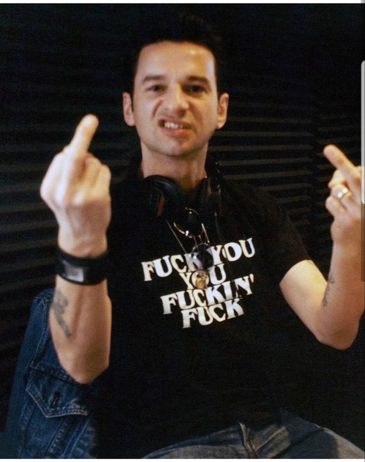 a man sitting down with his fingers up in the air and wearing a black shirt