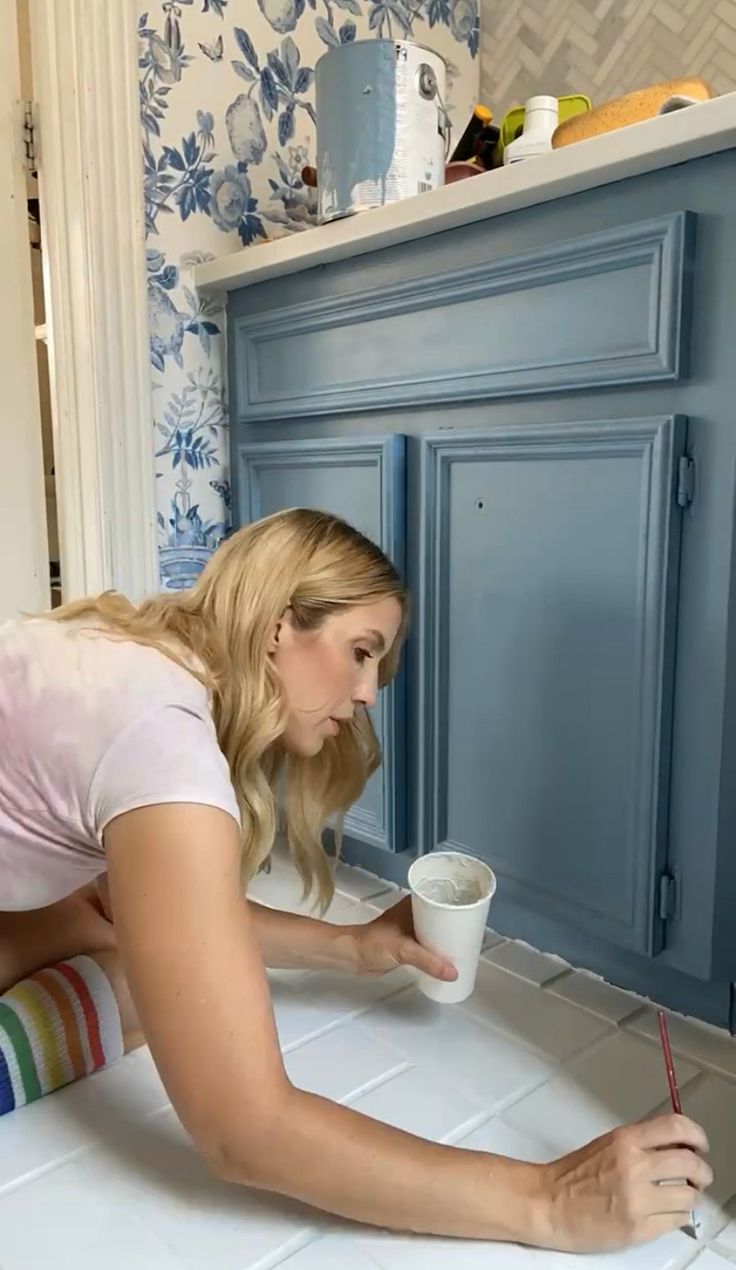 a young woman is painting the walls in her kitchen with blue and white wallpaper