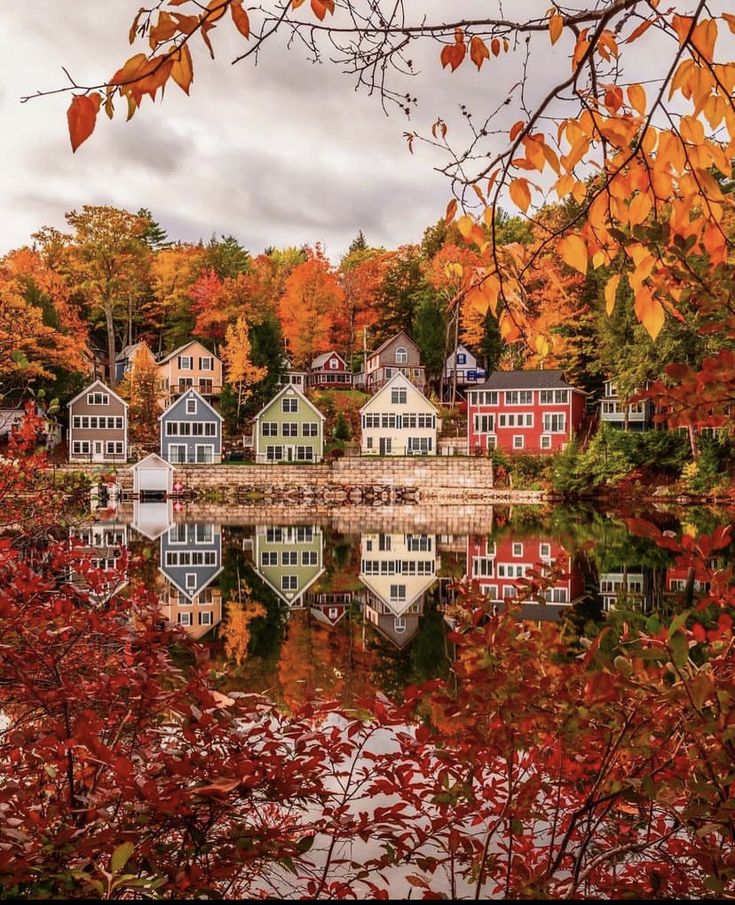 colorful houses are reflected in the still water of a lake surrounded by trees with autumn foliage