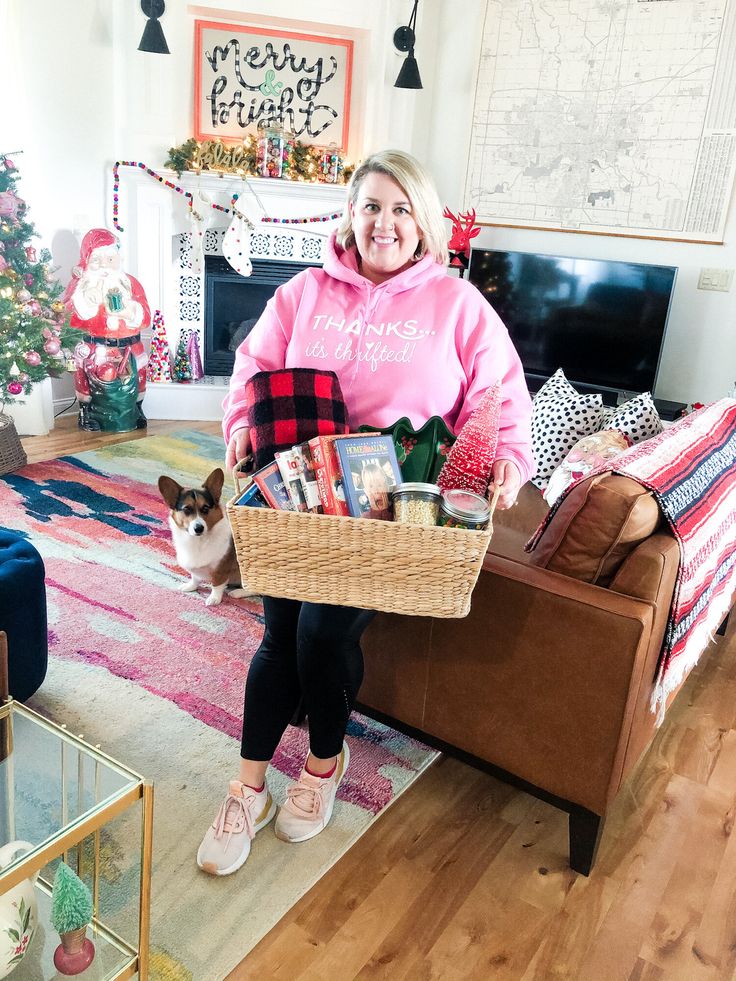 a woman sitting on a couch holding a basket filled with books and magazines in front of a christmas tree