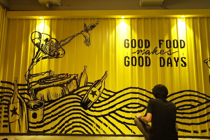 a man sitting on the floor in front of a yellow wall with words painted on it