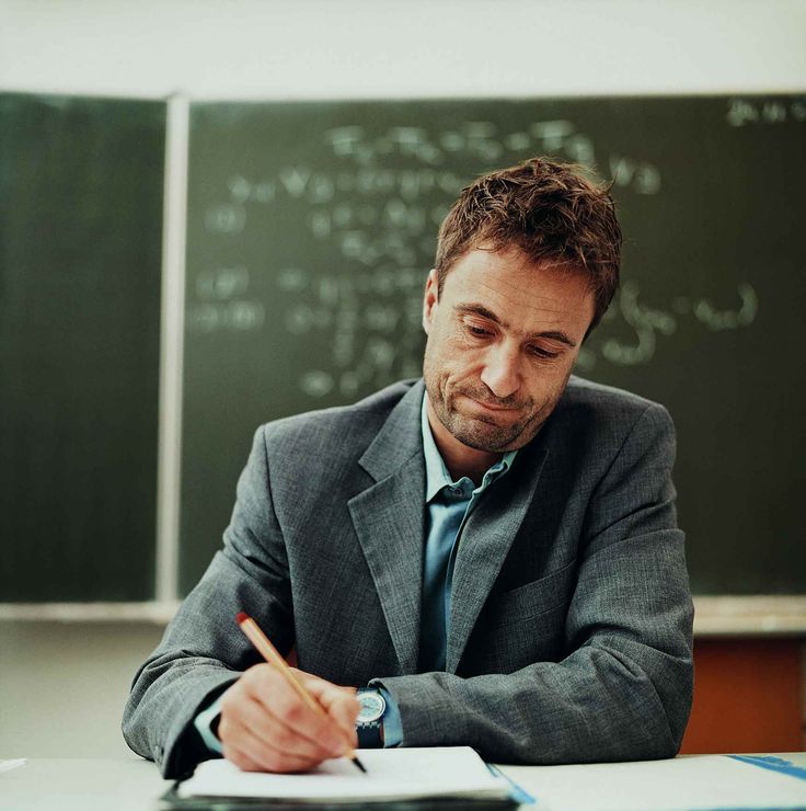 a man sitting at a desk in front of a blackboard with writing on it