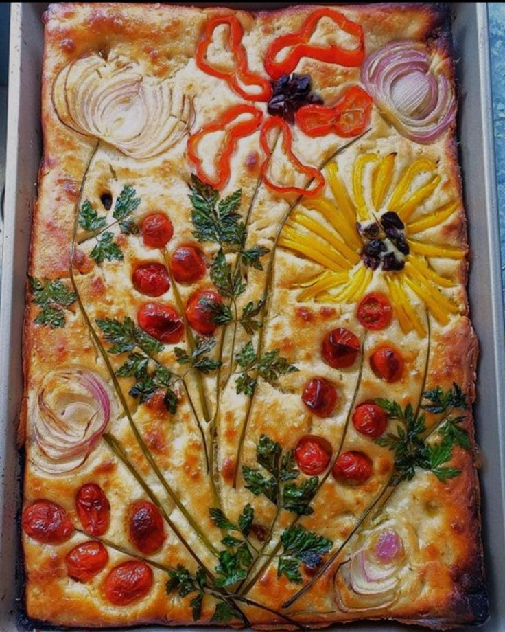 a square pizza with tomatoes, onions and other toppings in a baking pan on a table