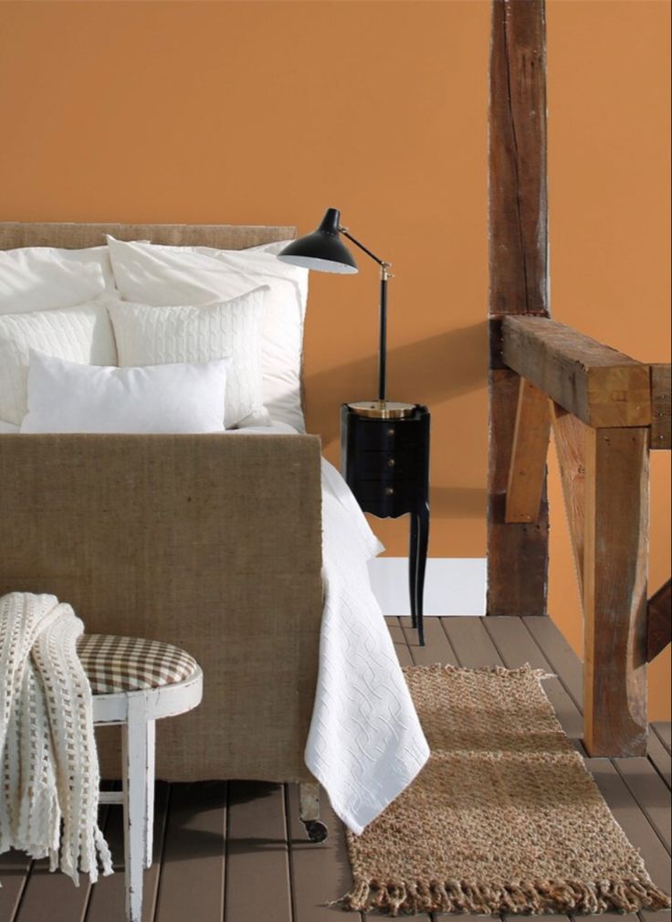 a bedroom with an orange accent wall and white bedding, rugs and chairs