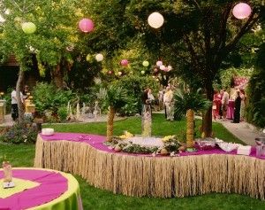 a lush green yard with pink and yellow decorations on the table, surrounded by palm trees