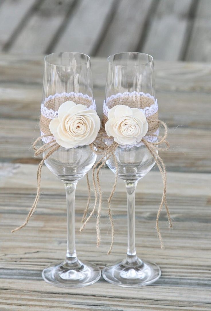 two wine glasses decorated with white roses and burlocks on a wooden table top