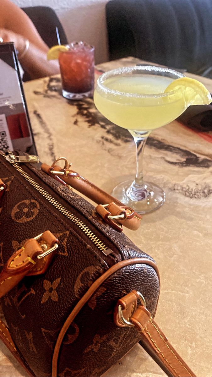 a brown purse sitting on top of a table next to a drink and laptop computer