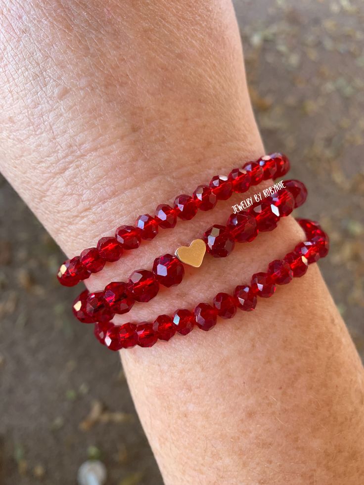 two bracelets with red beads and gold hearts on the wrist, one has a heart charm