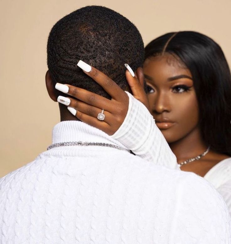 a man and woman embracing each other in front of a beige background with white nail polish on their nails