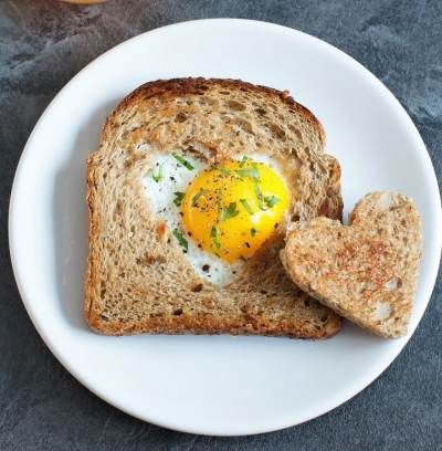 an egg in the middle of bread on a white plate with two pieces of heart shaped toast