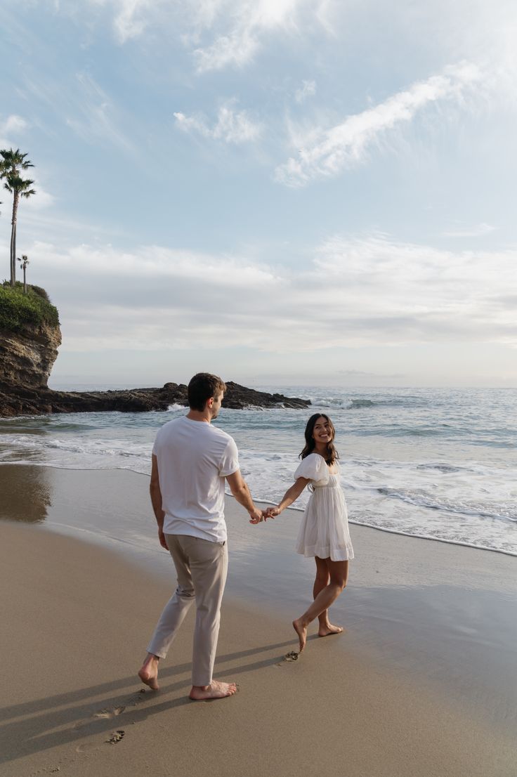 a man and woman holding hands walking on the beach with palm trees in the background