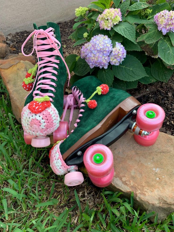 a pair of pink roller skates sitting on top of a rock next to flowers