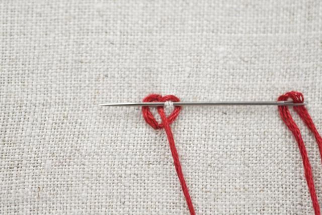 two crochet hooks with red yarn on them sitting next to each other in front of a white cloth