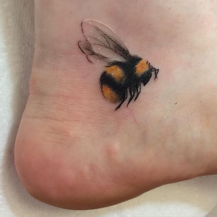 a small bee tattoo on the foot of a person's left foot, with an orange and black stripe