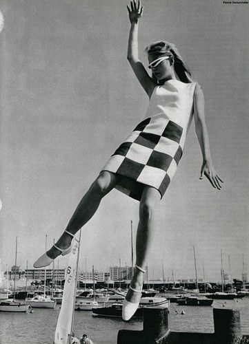 a woman is jumping in the air on a skateboard with boats in the water behind her