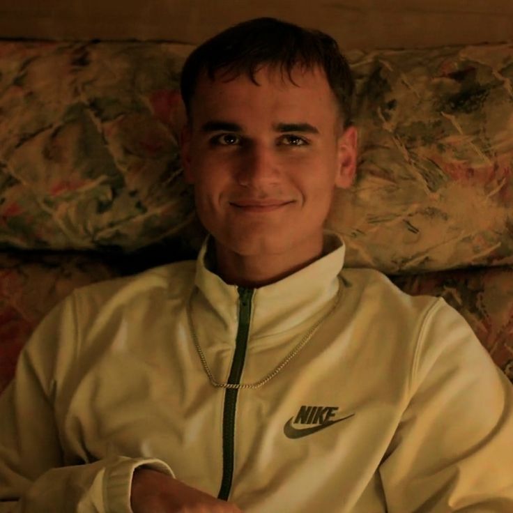 a man sitting on top of a couch wearing a white shirt and green nike jacket