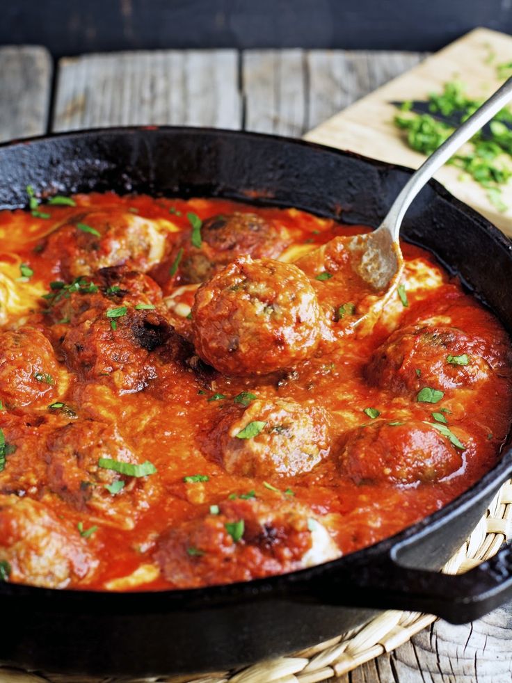 a skillet filled with meatballs covered in sauce and garnished with parsley