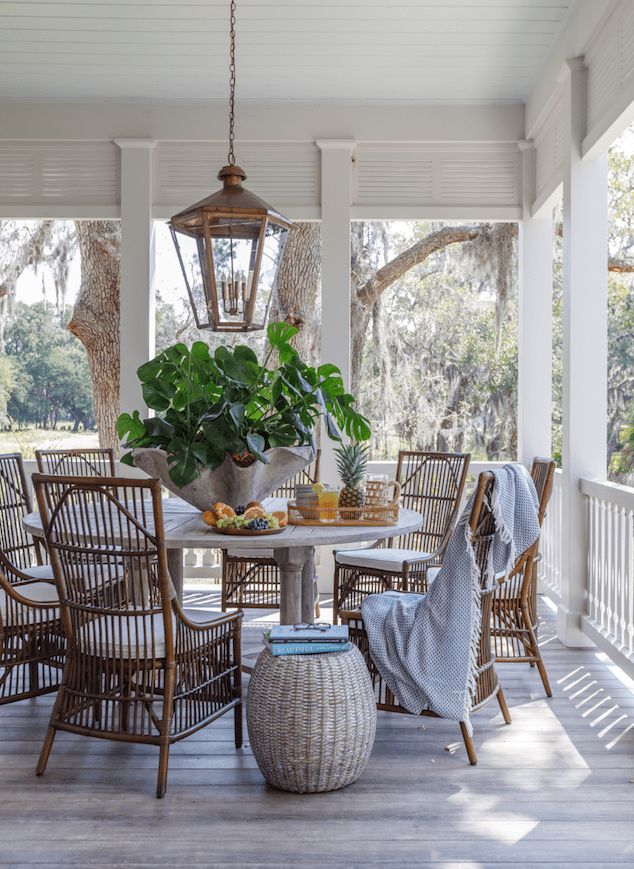 an outdoor dining area with wicker chairs and a round table surrounded by potted plants