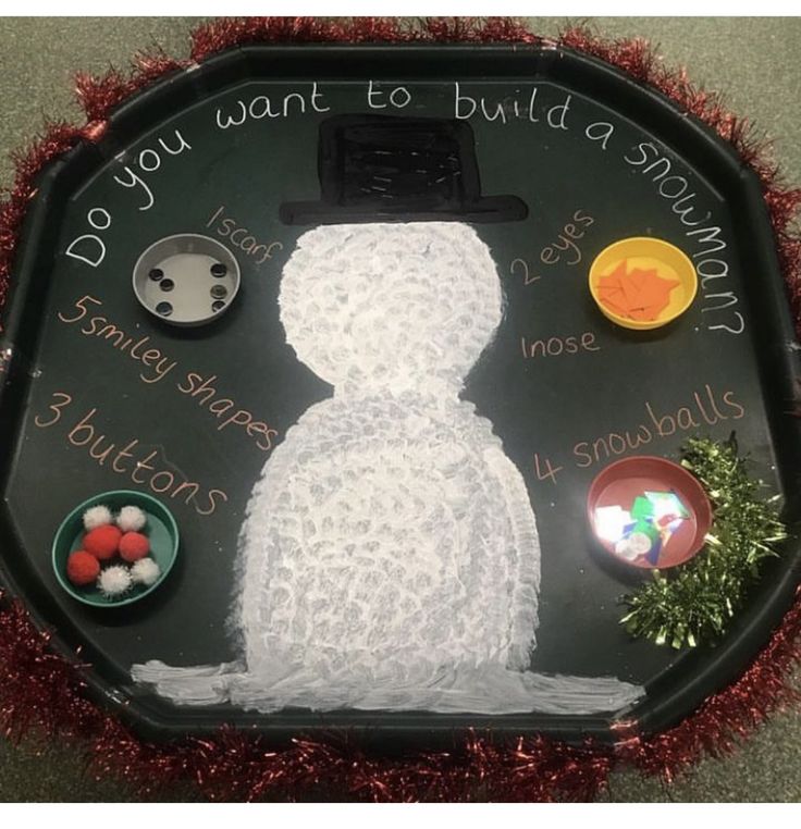 a snowman made out of buttons on a black tray with red tinsels