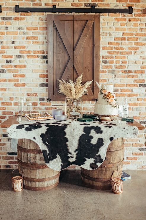 a table with a cow print cloth on it in front of a brick wall and wooden door