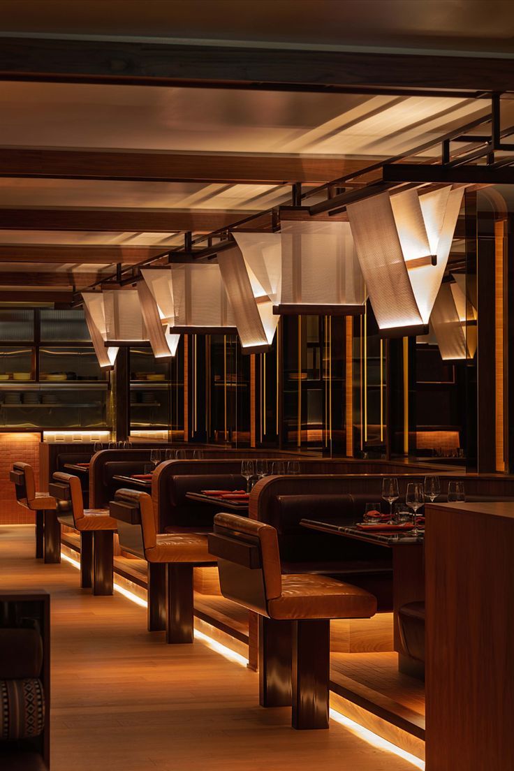 an empty restaurant with wooden benches and lights hanging from the ceiling above it, along with other seating areas