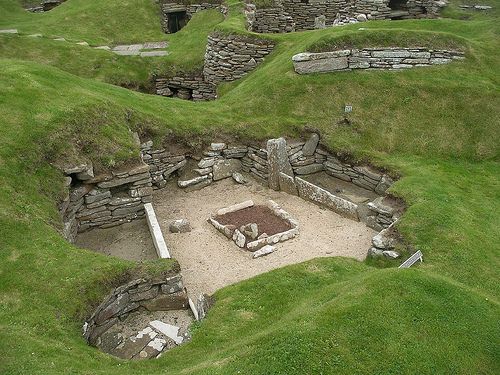 an old stone building with grass growing on the ground and rocks in the middle, surrounded by green grass