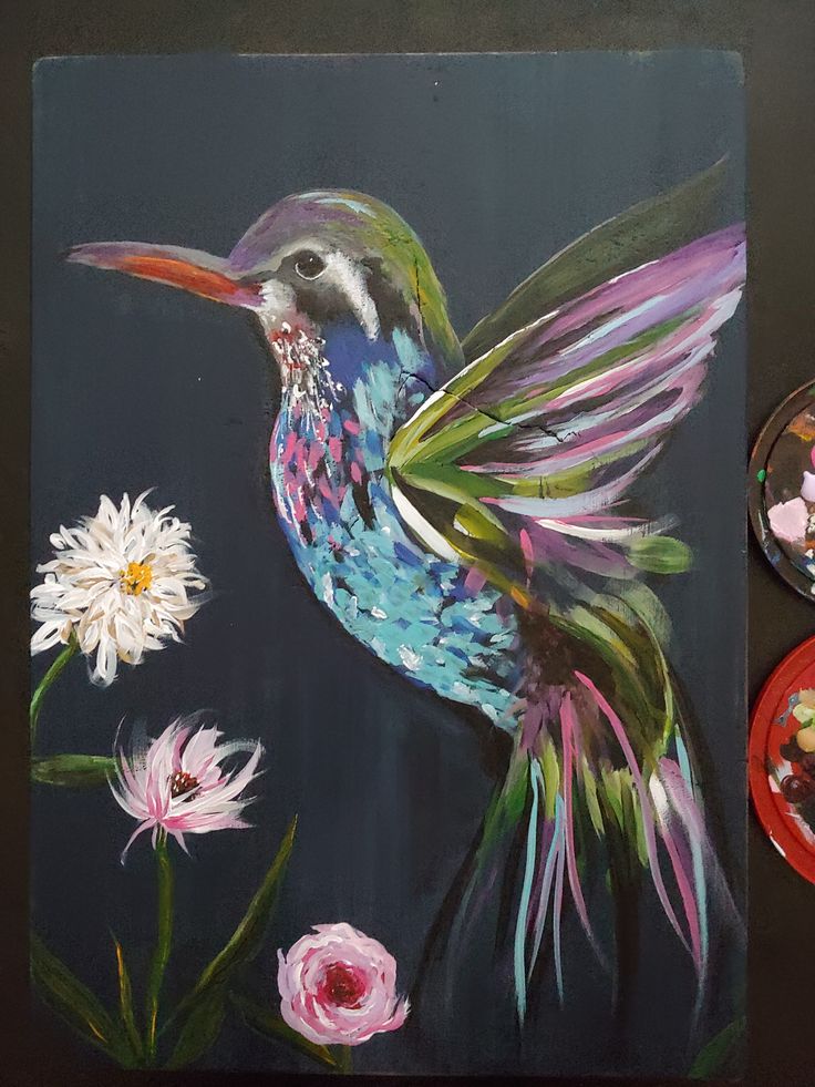 a painting of a hummingbird on a black background next to flowers and paintbrushes