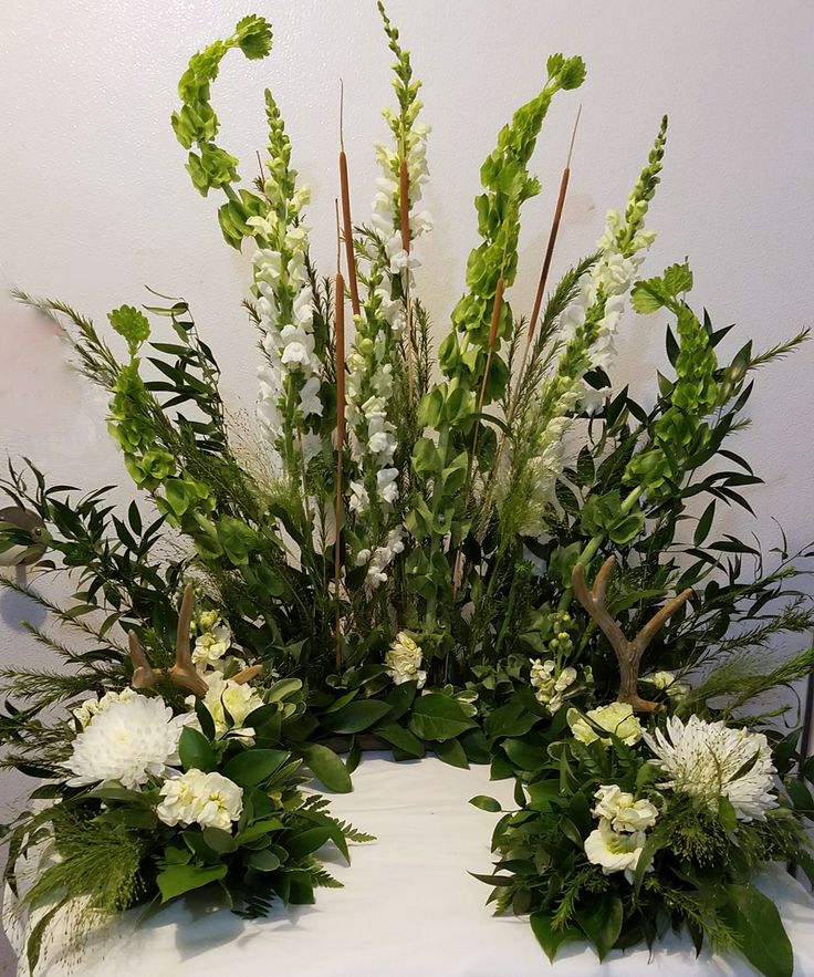 an arrangement of white flowers and greenery on a table