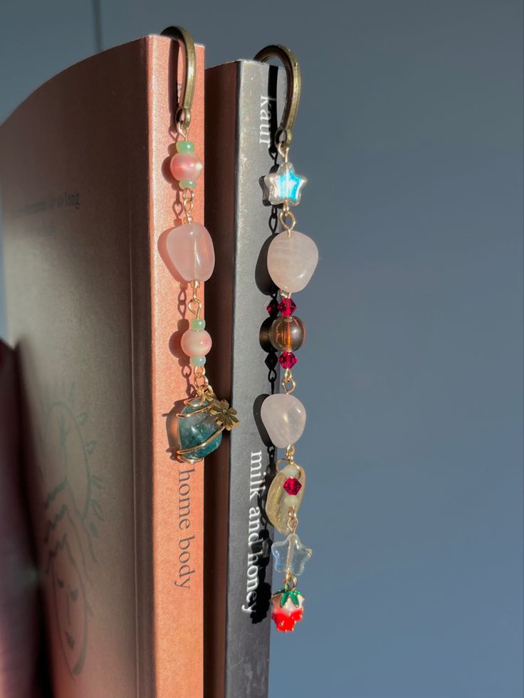 two bookmarks with charms attached to them sitting on top of an open bookshelf