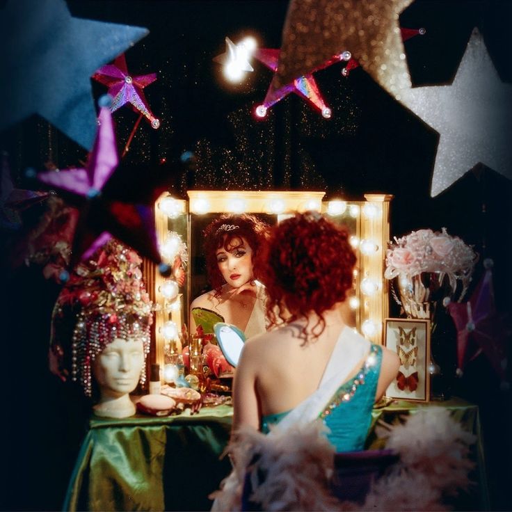 a woman looking at herself in the mirror with stars hanging above her and behind her