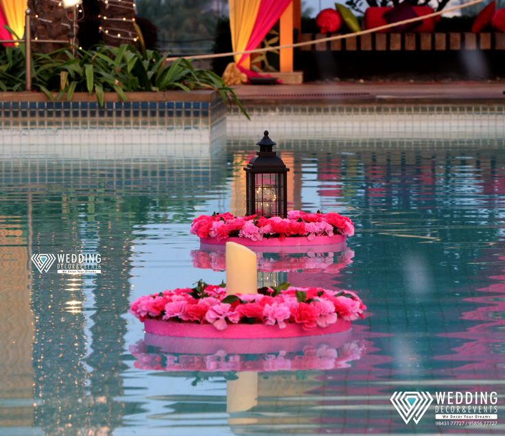 two floating candles with pink flowers on them in the middle of a pool at a wedding