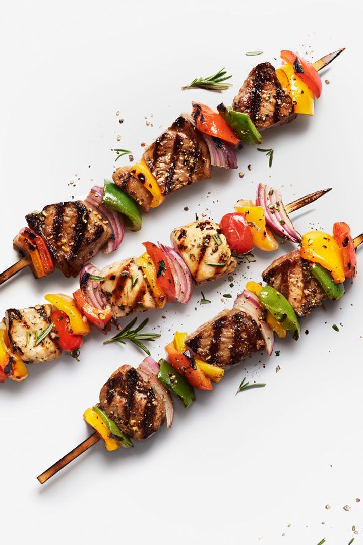 several skewers of meat and vegetables on a white surface