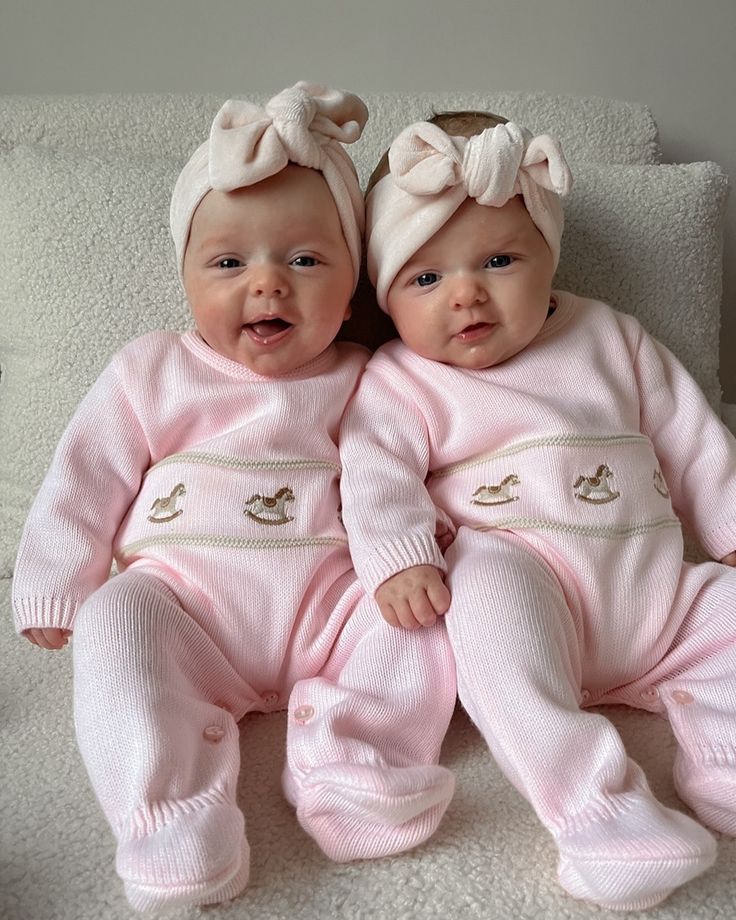 two baby babies laying on top of a white bed next to each other wearing pink outfits