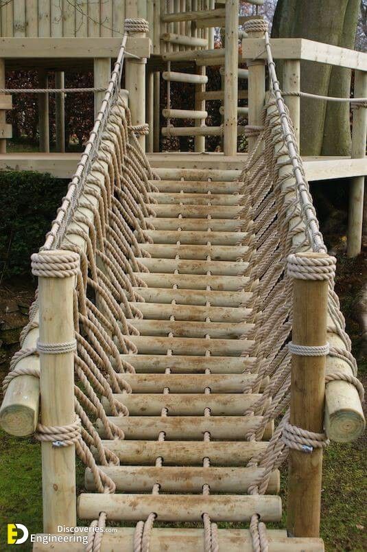 a rope bridge made out of logs and ropes with a wooden structure in the background