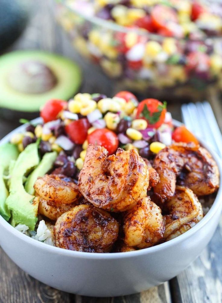 shrimp salad with avocado, corn and tomatoes in a white bowl on a wooden table