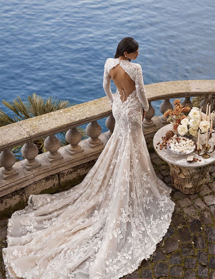 a woman in a wedding dress standing on a balcony looking at the ocean from behind