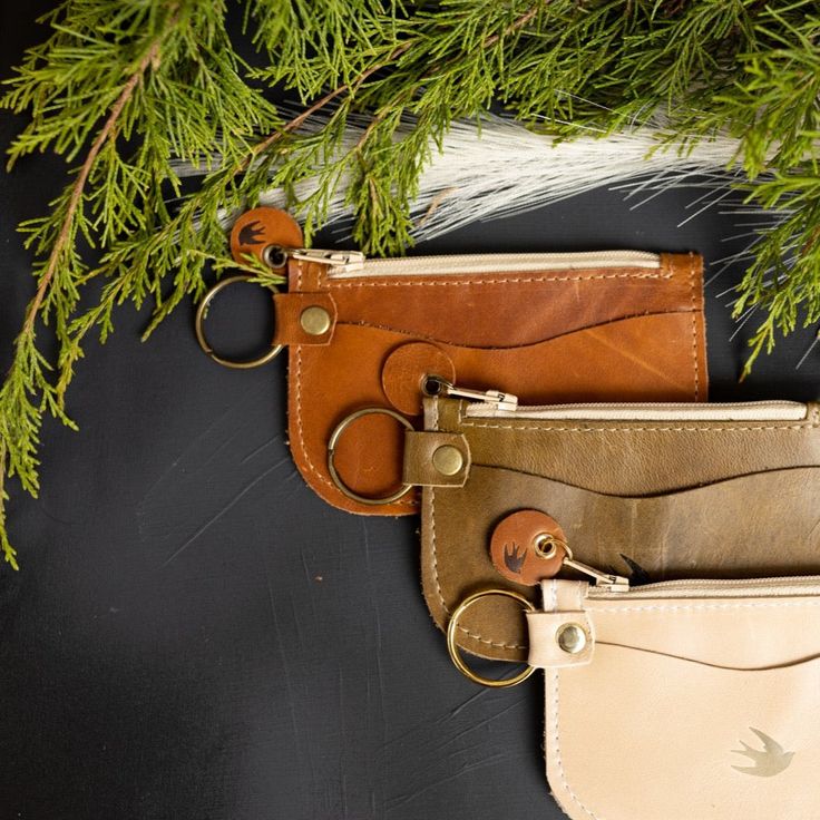 two leather wallets with key chains hanging from them next to a tree branch on a black background