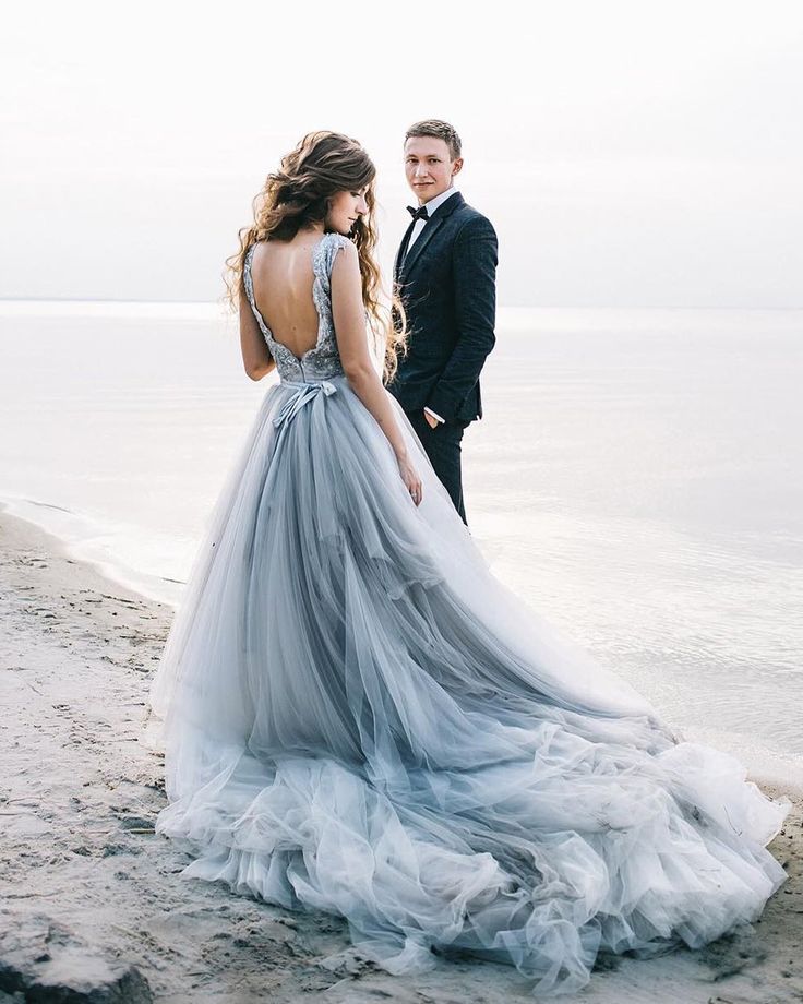 a man in a tuxedo standing next to a woman wearing a dress on the beach