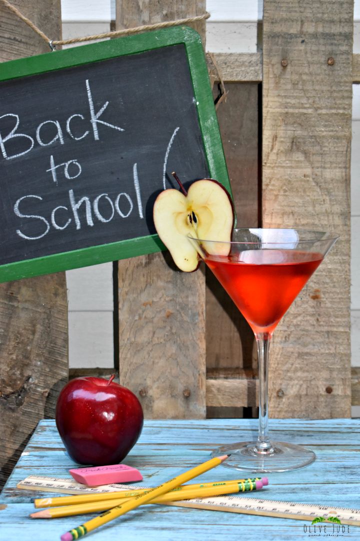 an apple sitting on top of a wooden table next to a glass filled with liquid