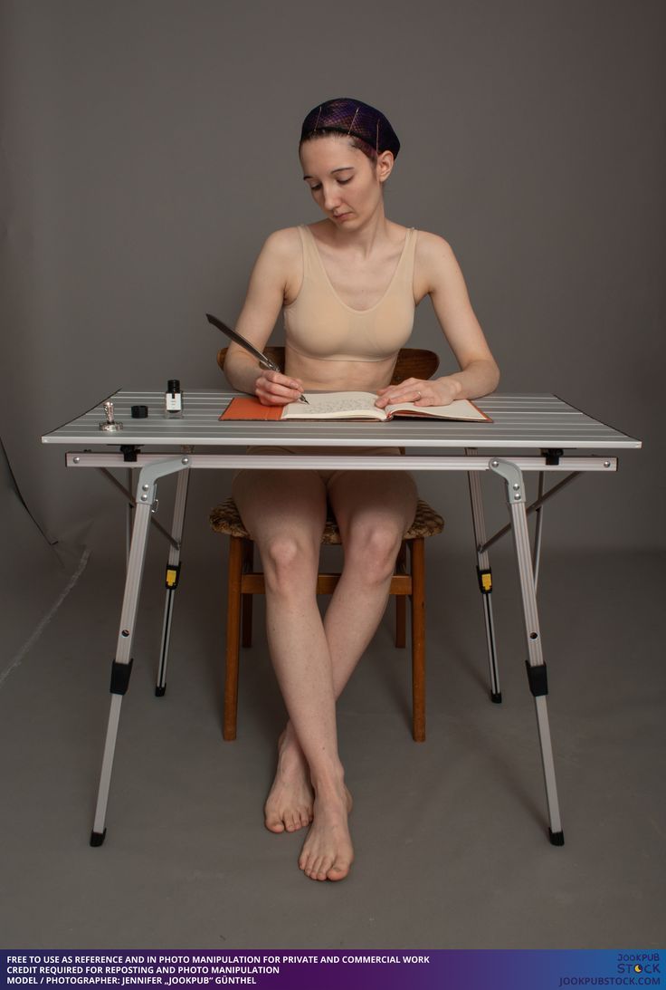 a woman sitting at a table with an open book and pen in her hand while writing