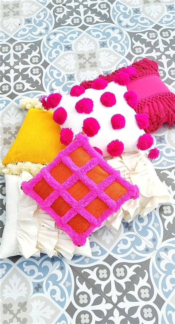 three different colored pillows sitting on top of a patterned table cloth with pom - poms