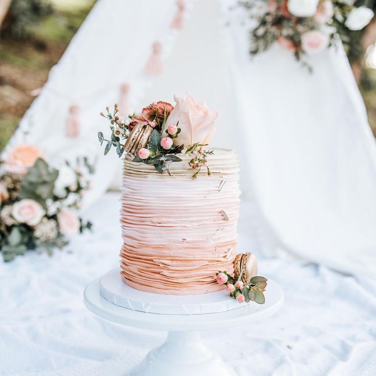 a wedding cake with pink icing and flowers on top sitting on a white tablecloth