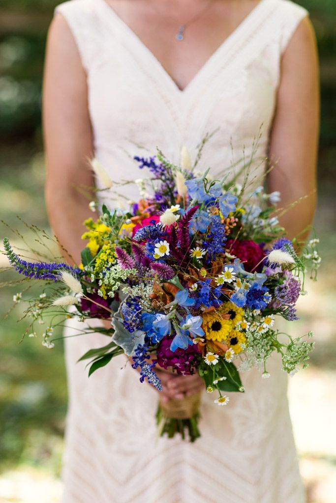 a woman holding a bouquet of flowers in her hands and wearing a white dress with purple, yellow and blue colors