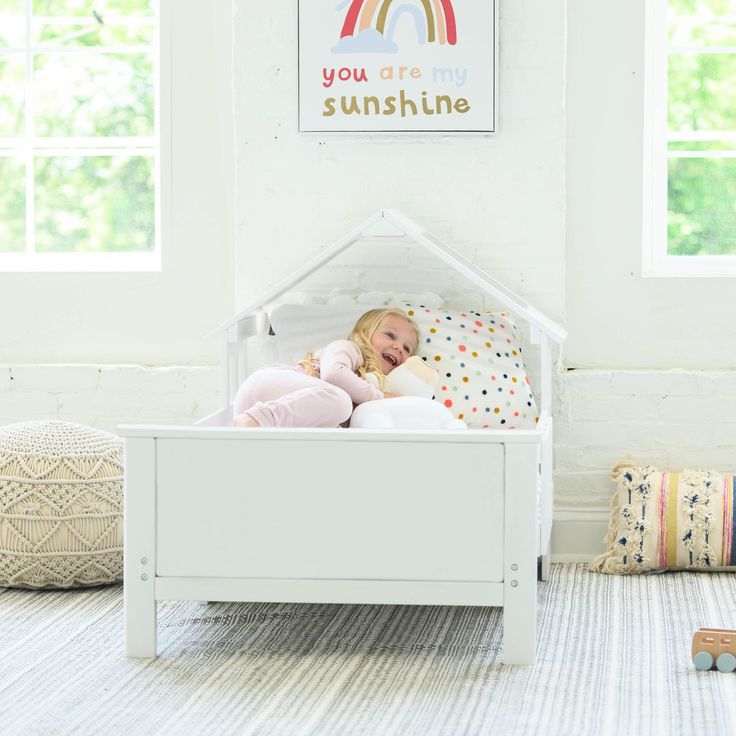 A young girl is laying in the Lil House Toddler Bed. House Bed For Kids, Kids Floor Bed, Toddler House, Toddler House Bed, Crib To Toddler Bed, House Beds For Kids, Ground Design, Floor Bed Frame, White Bunk Beds