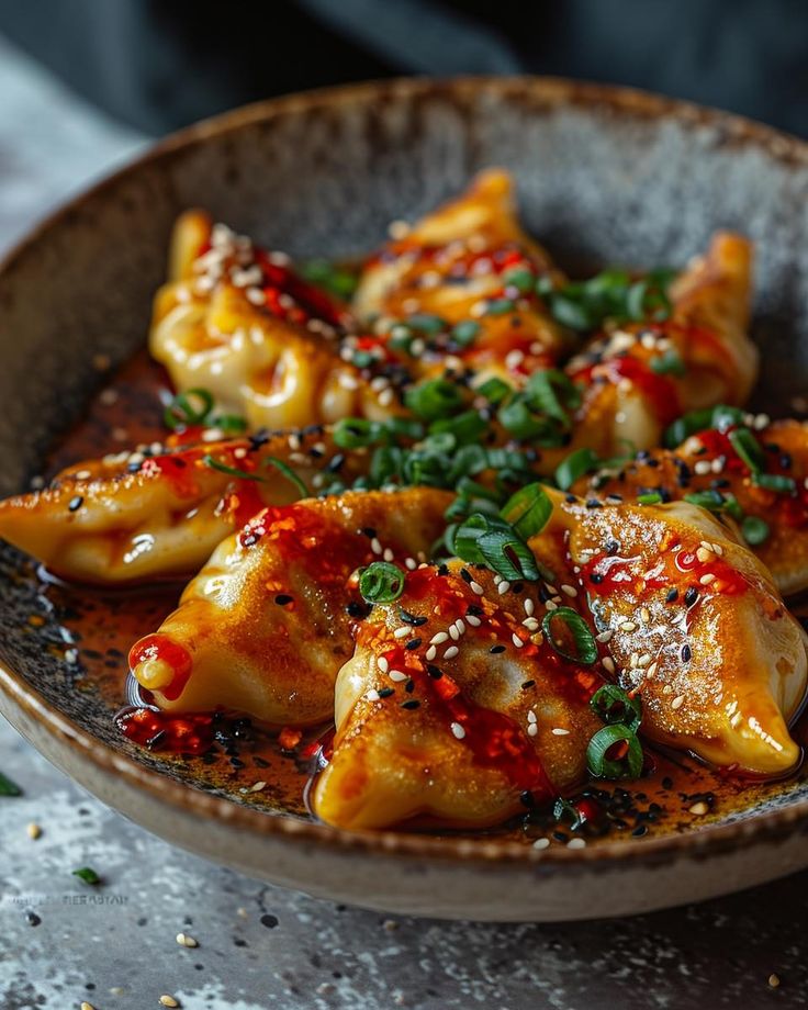 a bowl filled with dumplings covered in sauce and garnished with sesame seeds