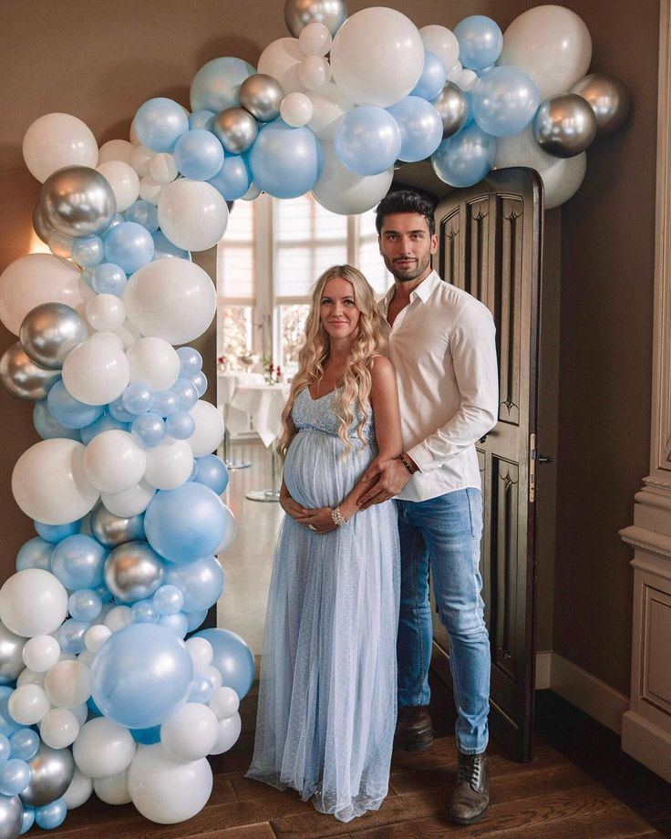 a man and woman standing next to each other in front of a blue and white balloon arch