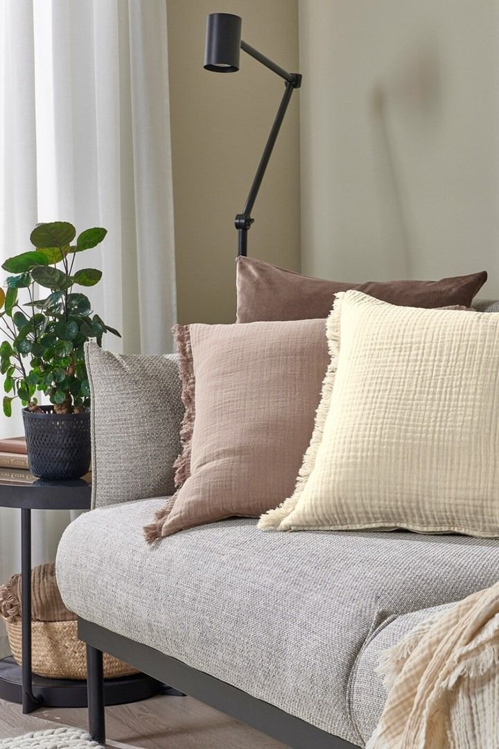 a couch with several pillows on it in front of a lamp and window sill