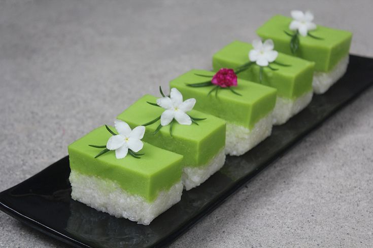 a black plate topped with four pieces of green cake covered in white and pink flowers